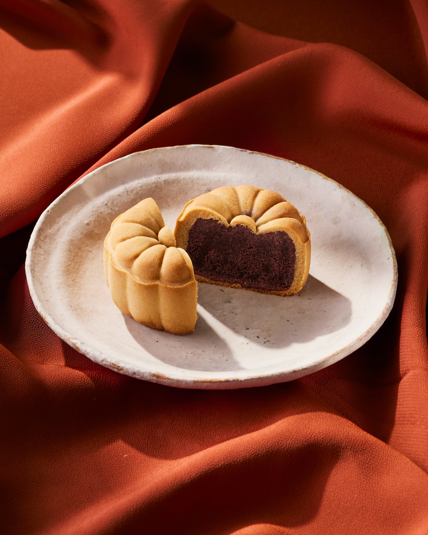 Red bean mini mooncake cut in half to show filling on a plate with a red cloth background