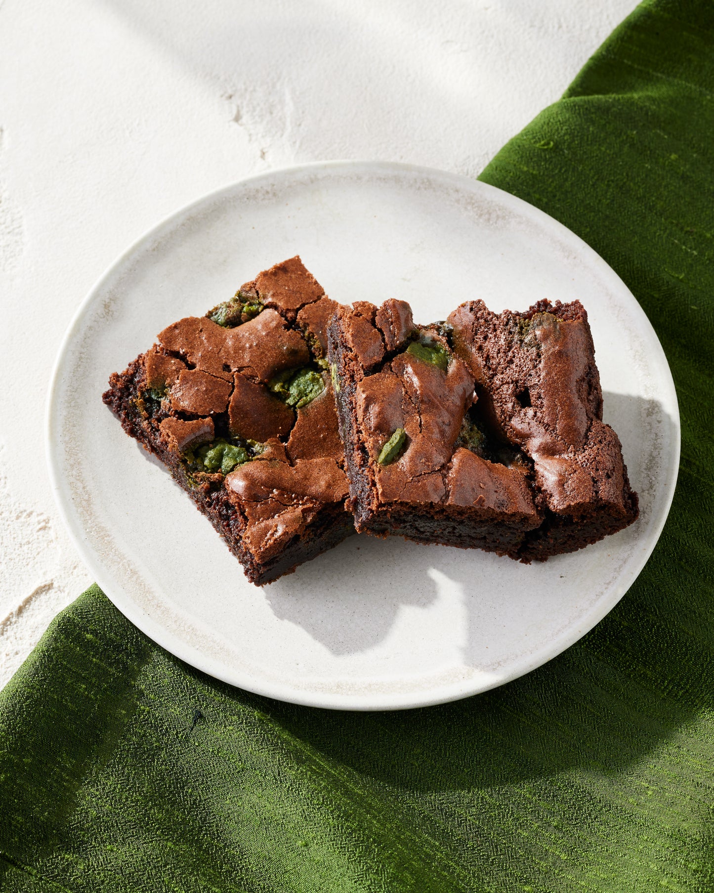 Two rectangle pieces of dark chocolate brownies with the matcha chocolate chunks peaking throughout the brownies.