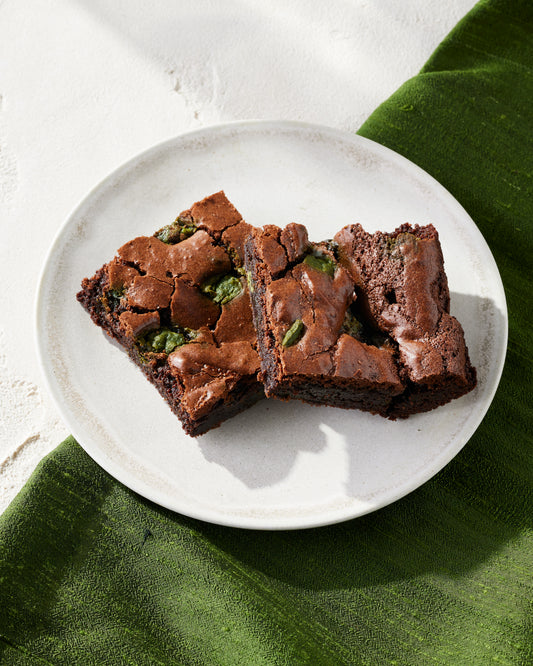 Two rectangle pieces of dark chocolate brownies with the matcha chocolate chunks peaking throughout the brownies.