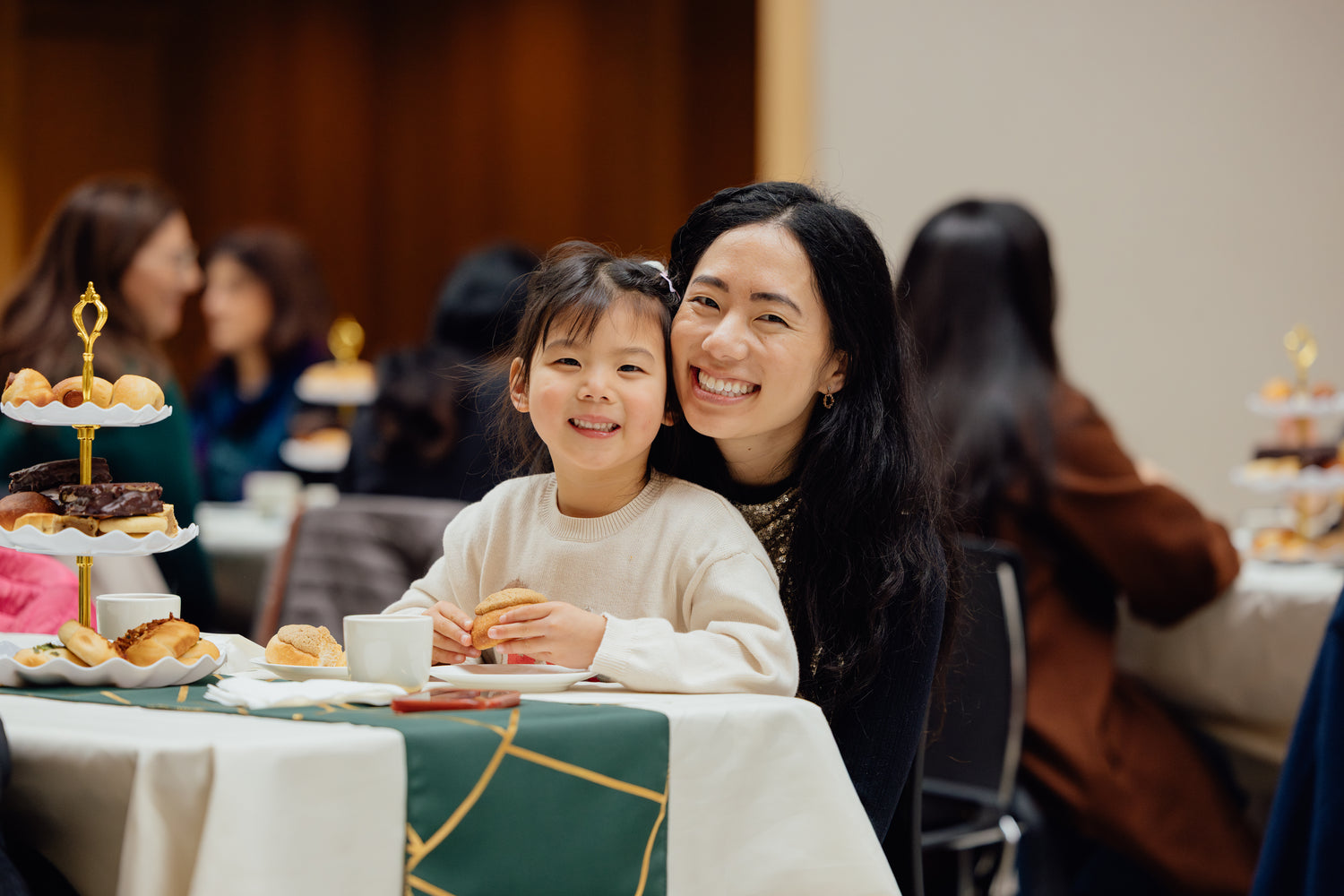 Woman and child sitting at a table with Asian pastries, smiling at the camera. Taken at Little Moon Bakehouse's Afternoon Tea service with Asian pastries.