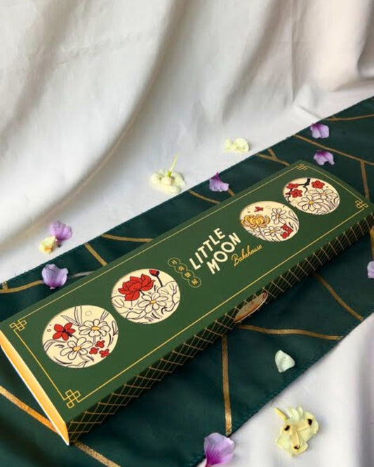 Green box with floral designs and 'Little Moon' branding on a white fabric background